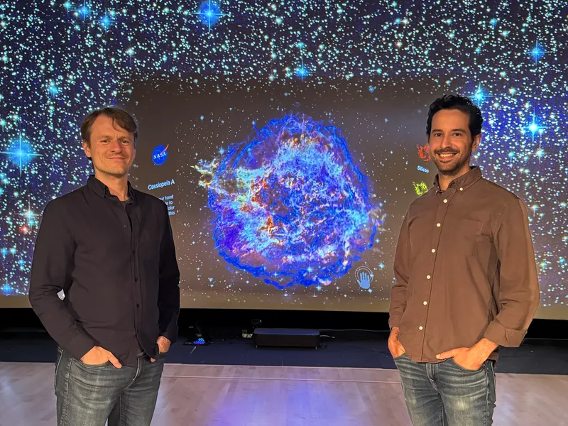 Picture of Matt and Andrew from System Sounds standing in front of their interactive sonification wall.