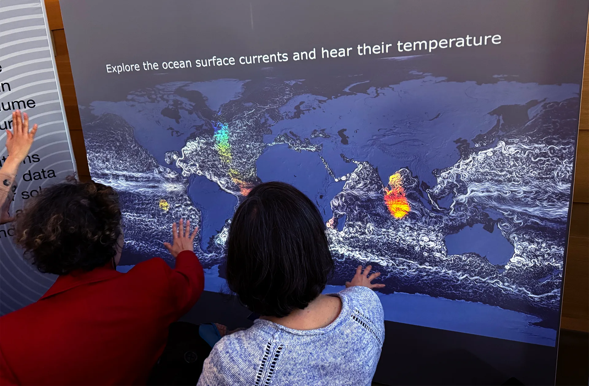 Photo of 2 adults their hands in front of interactive wall. The projected image displays ocean currents and temperatures.